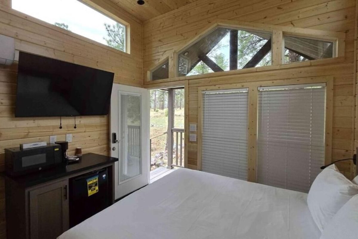 A wooden cabin room with a bed, a TV, a small desk, and a door leading outside.