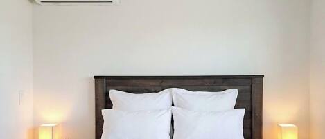 Hotelkamer met een bed, twee bedlampen, een plafondventilator, een airconditioner en een nachtkastje met een boek en een glas.