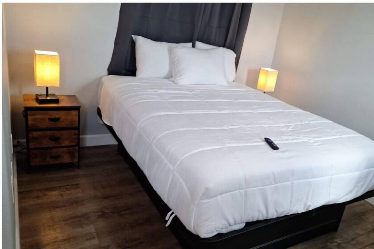 A single bed with a white duvet, a dark headboard, and two bedside lamps.