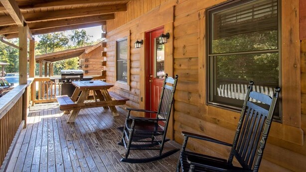 A wooden cabin with a deck, picnic table, rocking chairs, and a red door. - Wilderness Presidential Resort 2 Bedroom 2 Bathroom 1200 sq ft Log Cabin (Spotsylvania Courthouse)