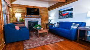 A cozy living room with wooden walls, a fireplace, a blue sofa, and a television. - Wilderness Presidential Resort 2 Bedroom 2 Bathroom 1200 sq ft Log Cabin (Spotsylvania Courthouse)