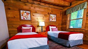 A wooden cabin-style room with two beds, a nightstand with a lamp, and framed artwork on the walls. - Wilderness Presidential Resort 2 Bedroom 2 Bathroom 1200 sq ft Log Cabin (Spotsylvania Courthouse)