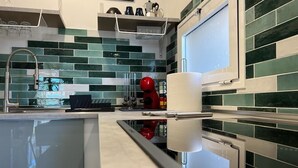 A modern kitchen with a reflective countertop, green and white tiles, a red appliance, and a white paper towel holder.