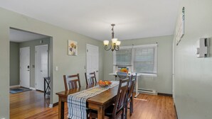A dining area with a wooden table, chairs, a chandelier, and a window with blinds.