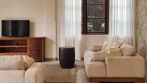 Una sala de estar con un sofá color beige, un mueble de madera con un televisor de pantalla plana, un reposapiés negro y una pared de piedra.