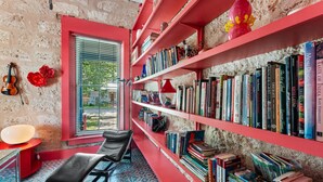 Eine gemütliche Leseecke mit einem roten Sessel, einem kleinen Tisch und einem Bücherregal voller Bücher.