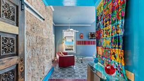 Ein Zimmer mit Steinwand, einem roten Sofa, einem gemusterten Boden, blauer Decke und einem farbenfrohen Wandteppich.