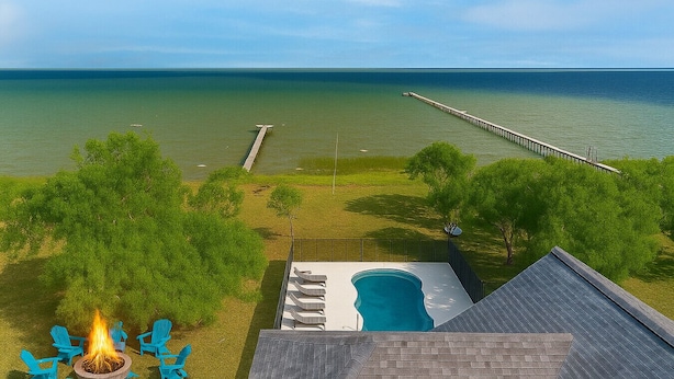 Un jardin avec une piscine, un foyer extérieur et une jetée qui s’avance dans l’eau.