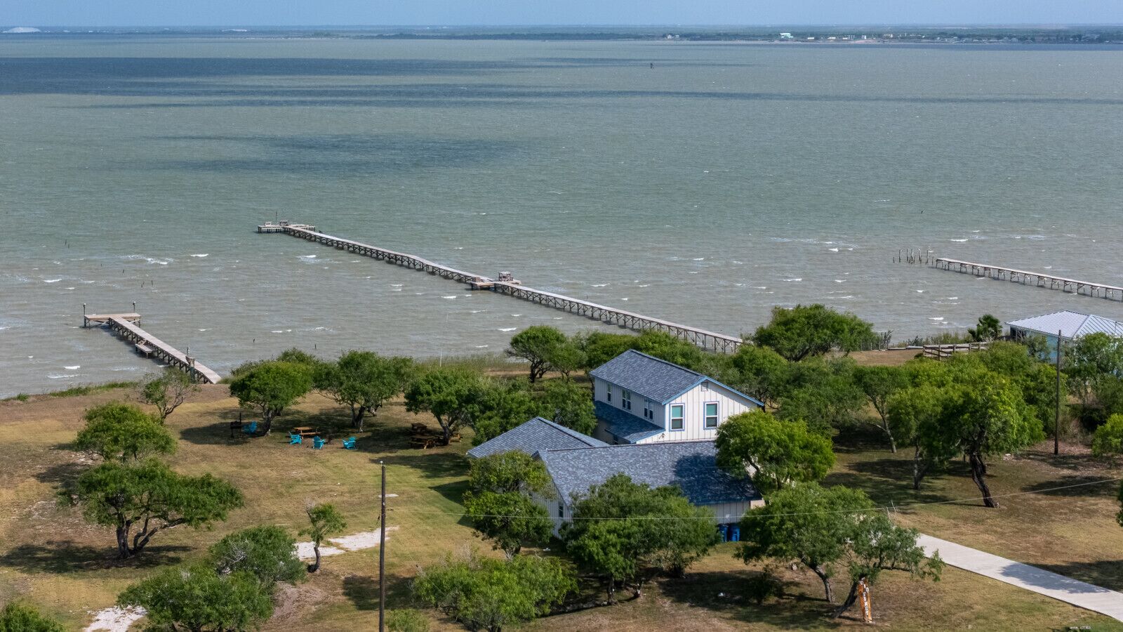 A coastal house with a dock extending into the water, surrounded by trees and a grassy area.