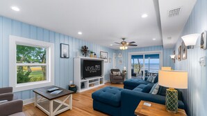 Un salon avec un canapé bleu, une table basse, un téléviseur et une vue sur l’extérieur.