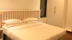 A neatly made bed with a wooden headboard, a bedside table, and a wardrobe with a mirror.