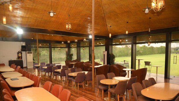 A spacious indoor dining area with wooden tables and chairs, large windows offering a view of a green landscape, and pendant lighting.