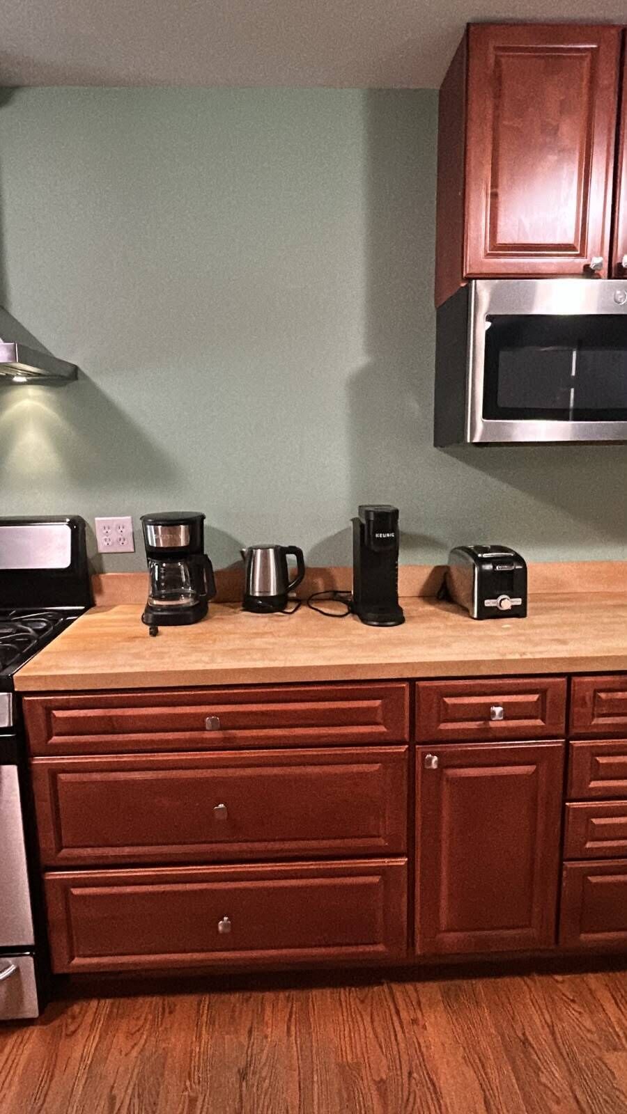 A kitchen with a wooden countertop, a coffee maker, a toaster, and a microwave.