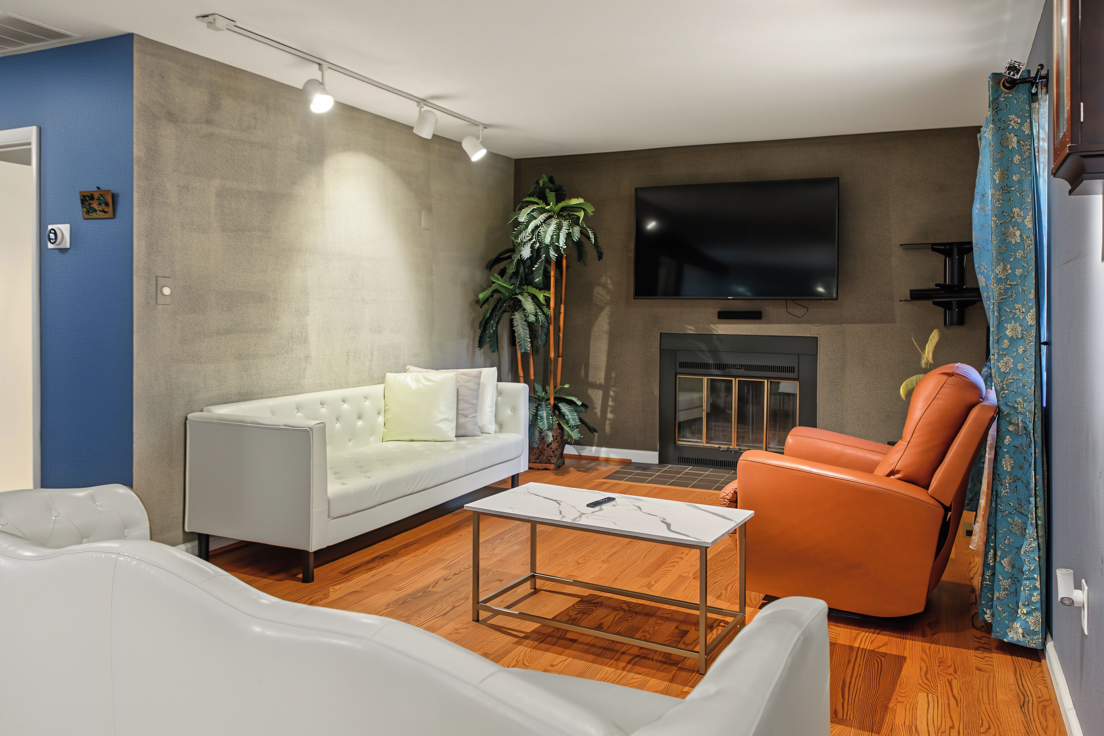 A modern living room with a white sofa, an orange armchair, a coffee table, and a flat-screen TV mounted on the wall.