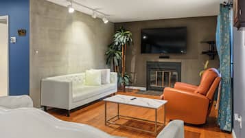 A modern living room with a white sofa, an orange armchair, a coffee table, and a flat-screen TV mounted on the wall.