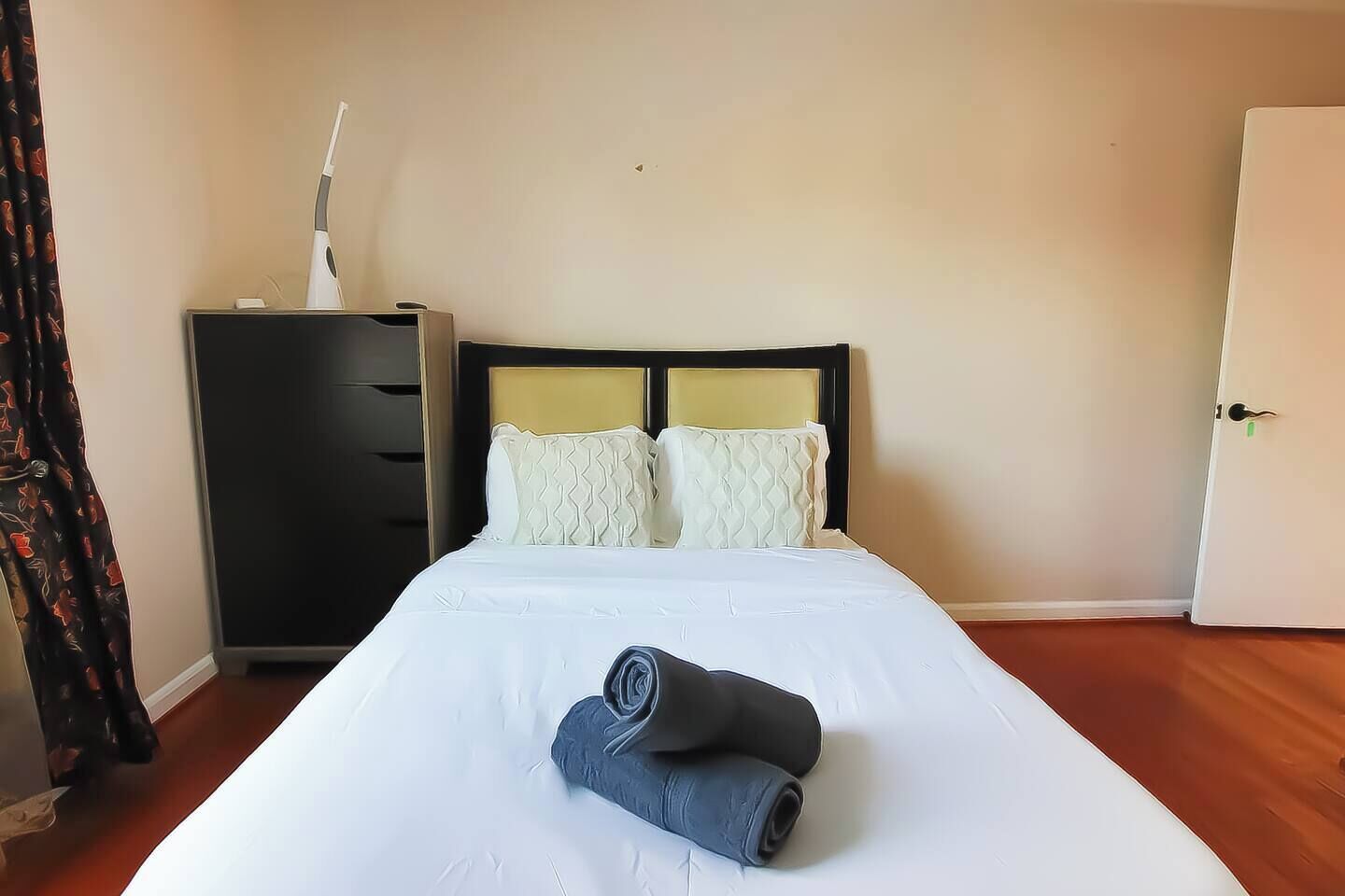 A neatly made bed with white linens, a rolled-up towel, and two decorative pillows.