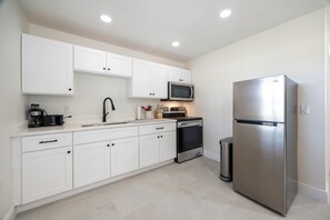 A modern kitchen with white cabinets, a stainless steel refrigerator, a microwave, a coffee maker, and a trash can. - Large efficiency with WiFi, AC, W/D less than 1 minute from WEC!!! (Ocala)