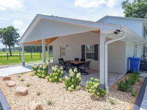 A covered outdoor patio with a table and chairs, surrounded by a garden with white flowers and pebbles. - Large efficiency with WiFi, AC, W/D less than 1 minute from WEC!!! (Ocala)