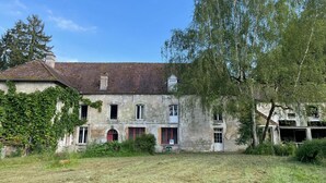 A rustic stone building with multiple windows and a sloped roof, surrounded by overgrown grass and trees. - Large party house, family or EVJ/G Ideal for get-togethers. (Loupeigne)