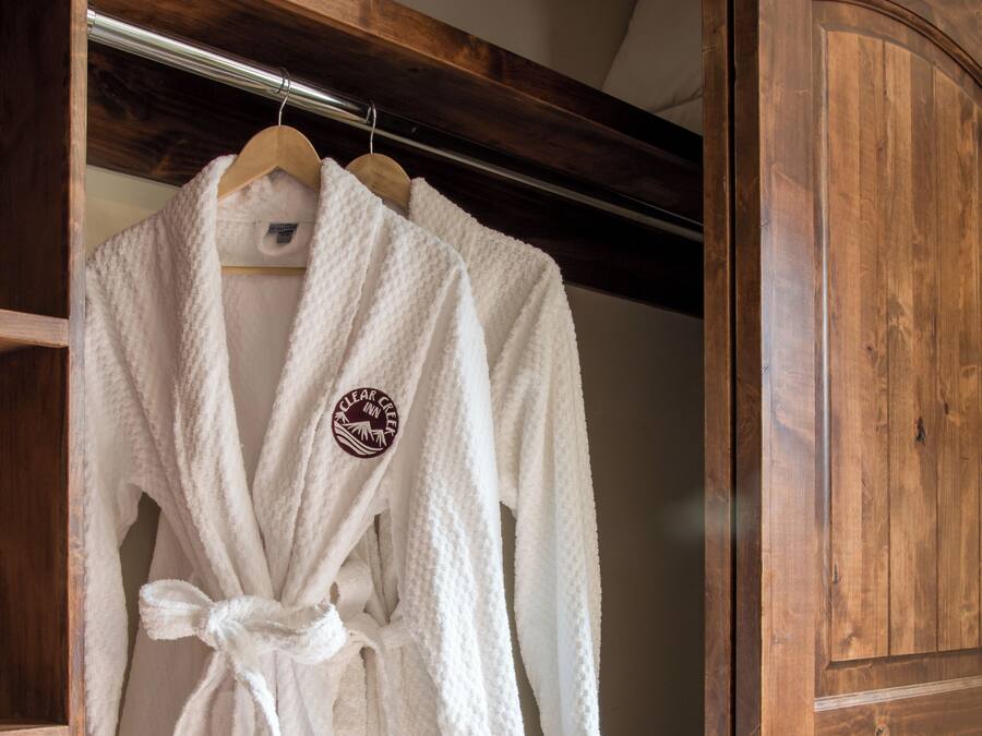 A white robe with a logo hanging on a wooden rack in a wooden closet.