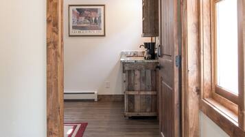 Un passage encadré de bois mène à une cuisine au décor rustique, avec un tableau encadré accroché au mur et un tapis rouge sur le sol.