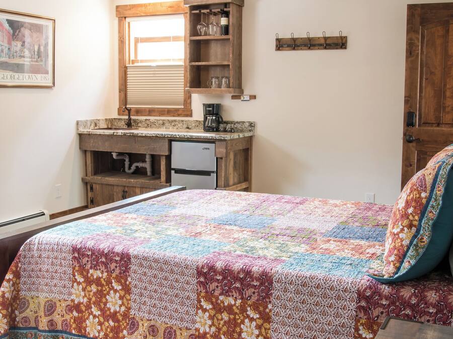 Quarto com cama de madeira, ventoinha no teto, cómoda de madeira, janela com persianas e quadro emoldurado na parede.