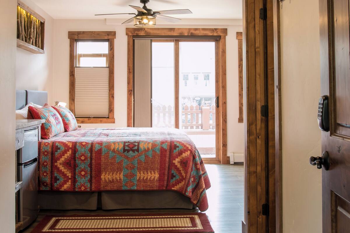 A bedroom with a bed, a ceiling fan, a window, and a door.