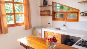 Cocina con una isla de madera, dos taburetes, una planta en maceta y una ventana con cortinas.