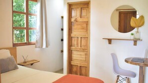 Un dormitorio con cama, escritorio con laptop, silla, puerta de madera y ventana con cortinas.