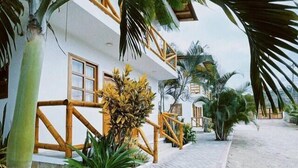 Una cabaña con un sendero pavimentado, palmeras y una valla de madera.