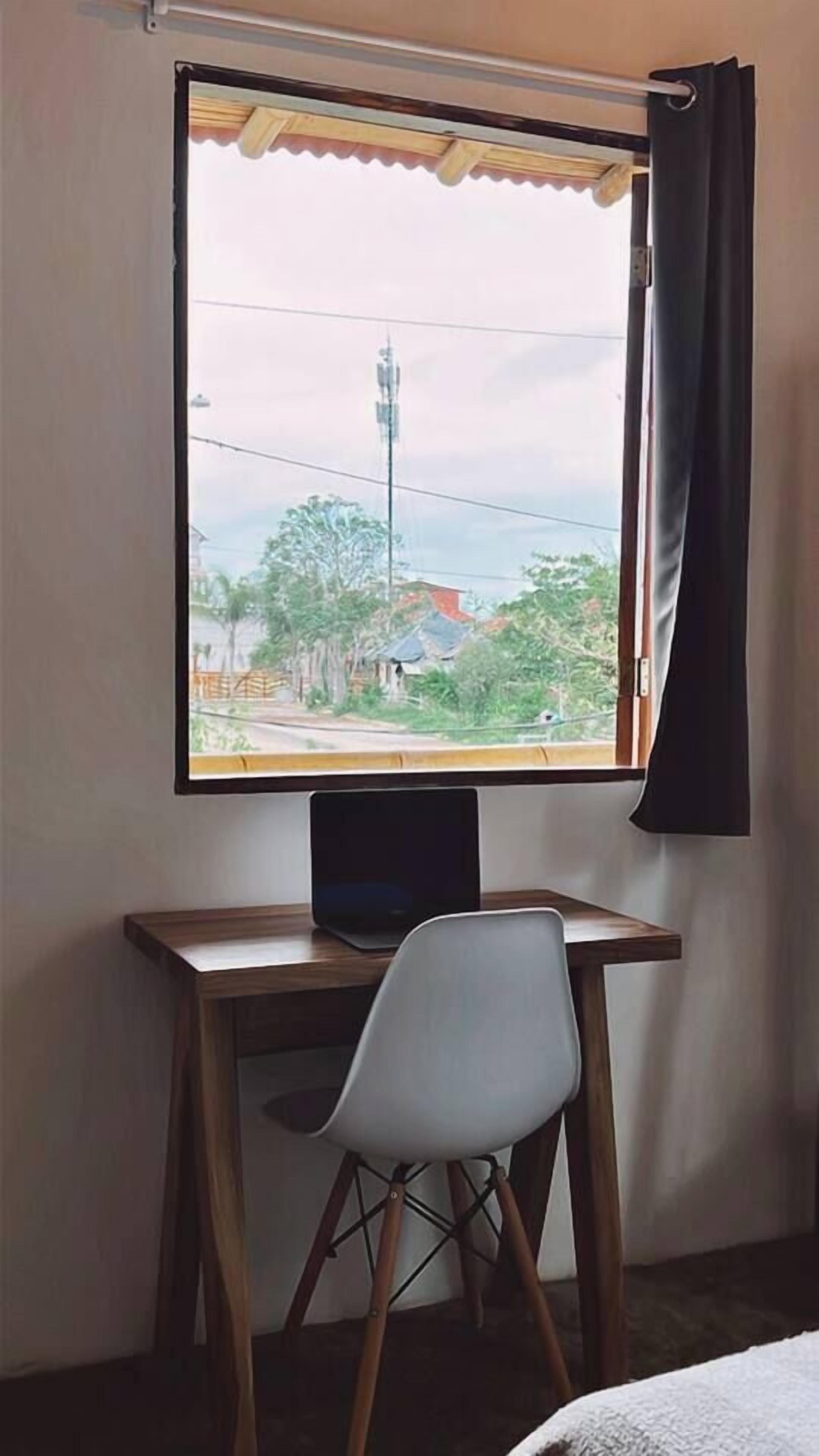 Ett rum med ett skrivbord, en stol och ett fönster med utsikt över en gata och byggnader.