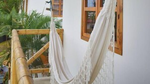 A hammock hanging from a wooden beam, a window with a wooden frame, and a balcony with a view of greenery.