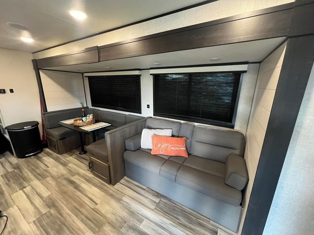 A compact RV interior with a sofa, a small table, and two windows.