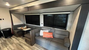 A compact RV interior with a sofa, a small table, and two windows. - Welcome to All Gussied Up, Glamping at the Gulf. (Port St. Joe)