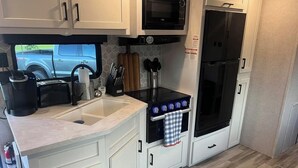 A compact kitchen with white cabinets, a microwave, a stove, and a refrigerator. - Welcome to All Gussied Up, Glamping at the Gulf. (Port St. Joe)