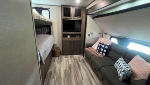 A compact RV interior with a bunk bed, a sofa, and built-in cabinets. - Welcome to All Gussied Up, Glamping at the Gulf. (Port St. Joe)