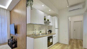 A modern kitchen with white cabinets, a wooden accent wall, a built-in oven, and a small island with a sink. - Elegance and comfort in San Giovanni, 3 minutes from metro and ideal for vacation. (Roma)