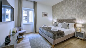 A modern bedroom with a large bed, a desk, a chair, a window with curtains, and a wall-mounted TV. - Elegance and comfort in San Giovanni, 3 minutes from metro and ideal for vacation. (Roma)