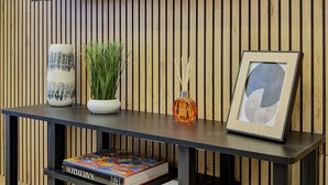 A modern room with a wooden slat wall, a dark console table, a vase, a potted plant, a bottle of reed diffuser, a framed picture, and a book titled "Sotheby's". - Elegance and comfort in San Giovanni, 3 minutes from metro and ideal for vacation. (Roma)