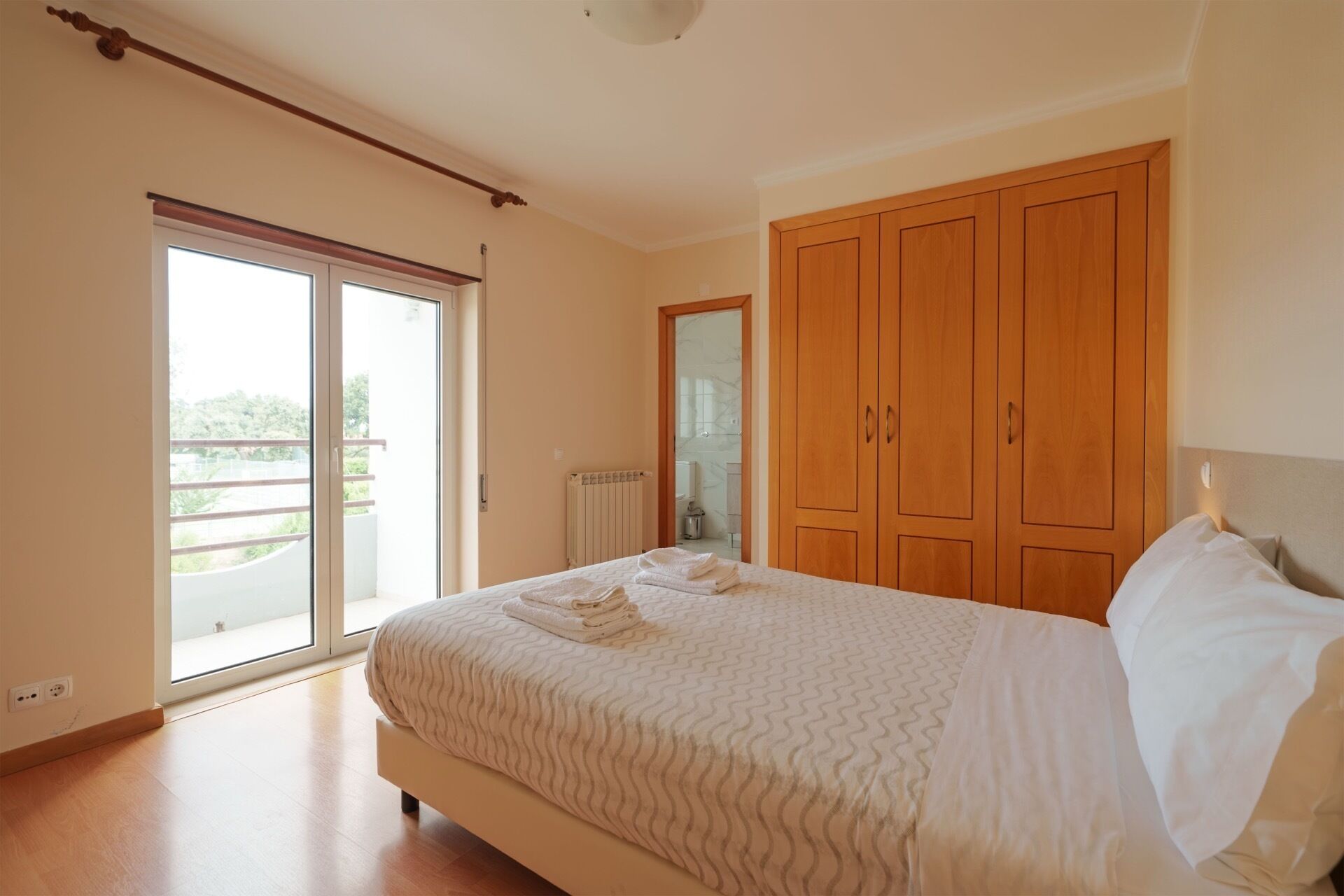 A bedroom with a large bed, a wardrobe, and a sliding glass door leading to a balcony.
