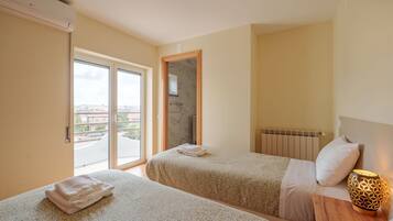 A hotel room with two beds, a radiator, a wooden nightstand with a lamp, and a sliding glass door leading to a balcony.