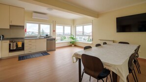 A modern kitchen with a dining area, large windows, and a flat-screen TV.