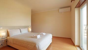 A hotel room with a large bed, bedside lamps, an air conditioning unit, and a window with a view.