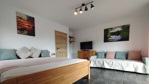 A bedroom with a wooden bed, a sofa, a TV, and artwork on the walls. - Vacation semi-detached house Tannenhuuske at the bathing lake Aurich-Tannenhausen East Frisia (Aurich)