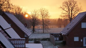 A residential area with houses featuring sloped roofs, a small shed, and a clear view of the sunset. - Vacation semi-detached house Tannenhuuske at the bathing lake Aurich-Tannenhausen East Frisia (Aurich)