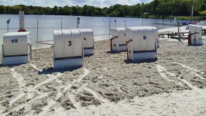 A beach with numbered beach chairs and a signpost in the foreground. - Vacation semi-detached house Tannenhuuske at the bathing lake Aurich-Tannenhausen East Frisia (Aurich)