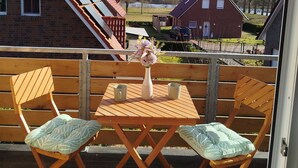 A wooden deck with two folding chairs and a table, a vase with flowers, and a view of houses and trees. - Vacation semi-detached house Tannenhuuske at the bathing lake Aurich-Tannenhausen East Frisia (Aurich)