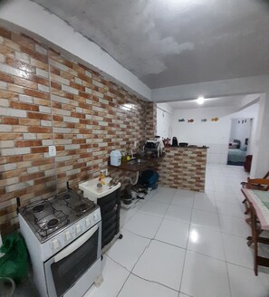 Una cocina con salpicadero de ladrillo, azulejos blancos, estufa a gas, lavamanos y zona de comedor con mesa y sillas.