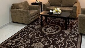 A living room with a sofa set, a coffee table with flowers, a lamp, and a painting on the wall. - AlShowaish Apartments (Taif)