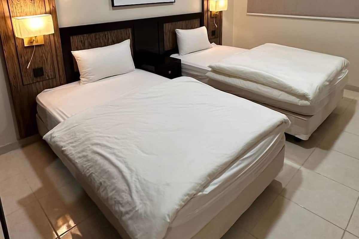 A hotel room with two beds, a framed artwork on the wall, and a nightstand with a lamp.